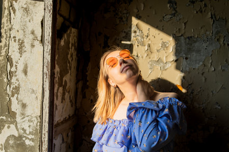 Bright Sunlight Shines Through Windows as Young Woman Poses in Abandoned Building During Golden Hour.の写真素材