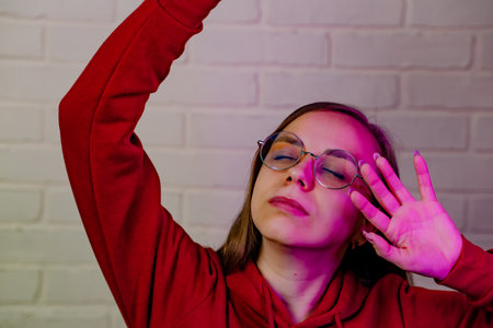 Woman Dancing Gracefully in Red Sweatshirt Against White Brick Wall at Evening.