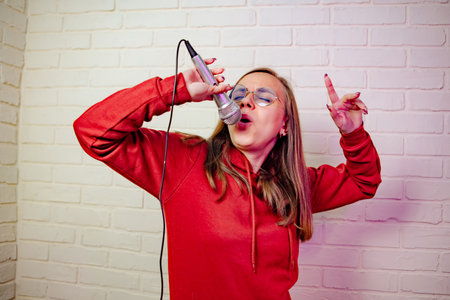 A woman in a red hoodie with a microphone in her hands sings and dances.
