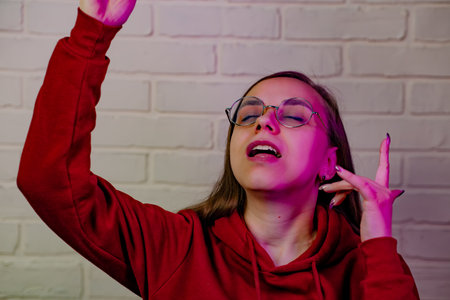 Woman Dancing Gracefully in Red Sweatshirt Against White Brick Wall at Evening.