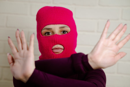 A woman wearing a bright pink balaclava dances energetically, striking unique poses with her hands...