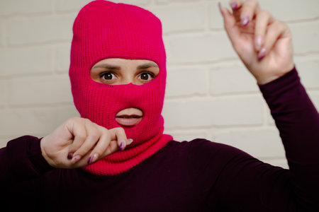 A woman wearing a bright pink balaclava dances energetically, striking unique poses with her hands...