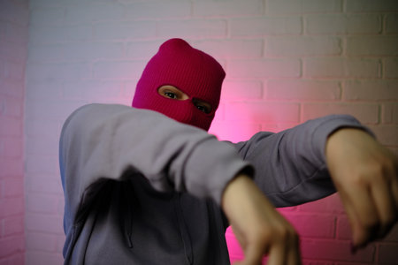 Individual in a pink balaclava poses against a colorful backdrop, making a gesture.の写真素材