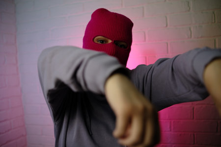 Individual in a pink balaclava poses against a colorful backdrop, making a gesture.の写真素材