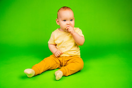 Toddler in Yellow Shirt Enjoys Eating a Piece of Liver on Green Background. A toddler bites into a...