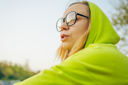Woman in a vibrant green outfit sitting thoughtfully on a hillside during sunset, enjoying nature in...