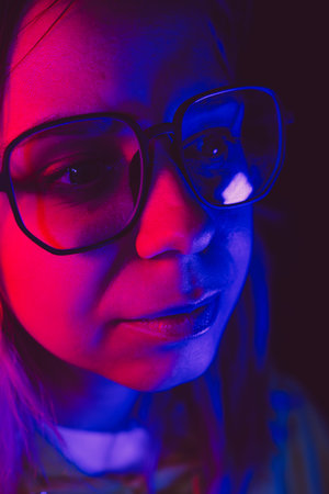 A woman with glasses illuminated by colorful lights on a dark night, creating a striking visual effect and mood.の写真素材