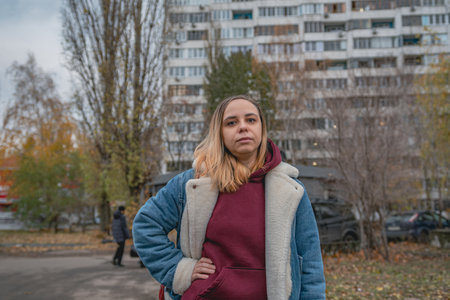 A young woman in casual outerwear strolls along a city street on a cool autumn day, surrounded by...