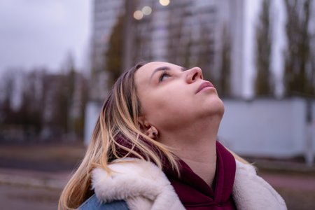 A young woman gazes thoughtfully upward amidst urban surroundings during early evening hours.の写真素材