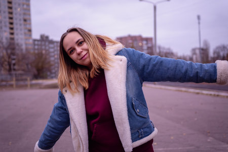 Young woman in casual attire stands in an urban environment during early evening, surrounded by tall...