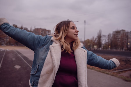 A woman stands with her arms wide open, enjoying the fresh air. The cloudy sky sets a moody backdrop as she strolls through an urban settingの写真素材