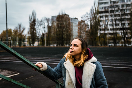 A young woman poses confidently on a staircase in an urban setting, showing her stylish winter outfit near residential buildings.の写真素材