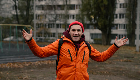 Excited person in orange jacket gestures enthusiastically outdoors in a city park during a cool day.の写真素材