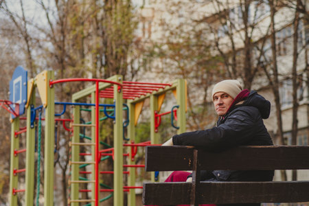 Man in winter coat reflects thoughtfully in urban park during cold afternoon.の写真素材