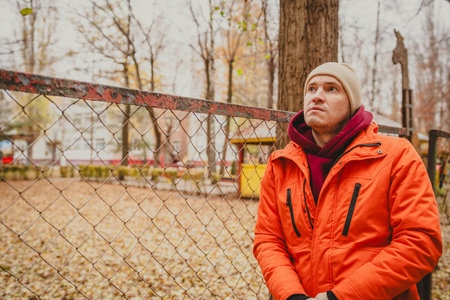 Casual portrait of a man wearing an orange jacket and beige beanie outdoors in an urban setting...