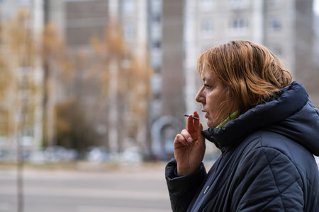 Woman enjoying a cigarette outside a building on a chilly day in a quiet urban atmosphere.の写真素材