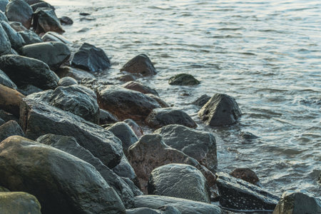 Smooth Stones Along a Serene Shoreline With Gentle Waves Lapping Against the Rocks During Early Morning.の写真素材