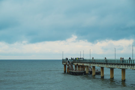 People Walking on a Pier Overlooking the Ocean at Dusk With Dramatic Clouds Above.の写真素材