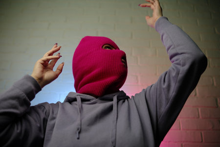 Individual in a pink balaclava poses against a colorful backdrop, making a gesture.の写真素材
