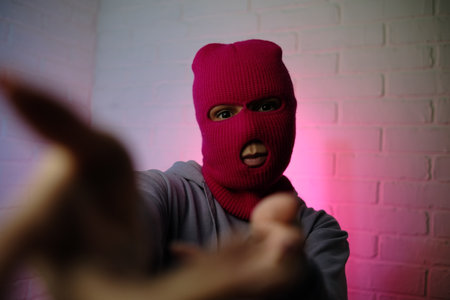 Individual in a pink balaclava poses against a colorful backdrop, making a gesture.の写真素材
