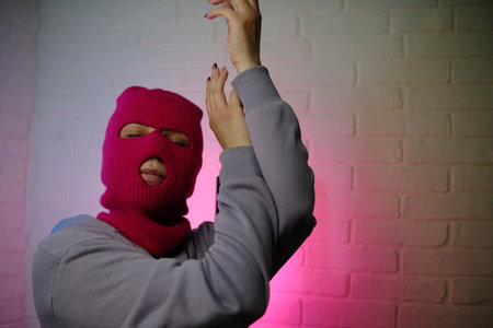 Individual in a pink balaclava poses against a colorful backdrop, making a gesture.の写真素材