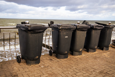 Multiple Black Trash Bins Lined Along a Seaside Promenade During a Cloudy Day.の写真素材