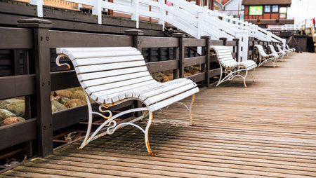 Benches Lined Along a Wooden Walkway by a Waterfront in a Quaint Coastal Town.の写真素材