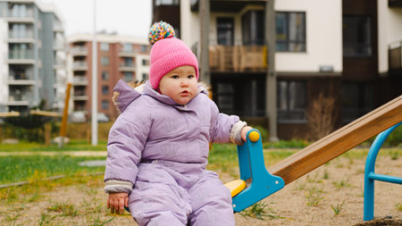Child Enjoys Playful Swing Time in a Colorful Park on a Chilly Day Surrounded by Modern Buildingsの写真素材