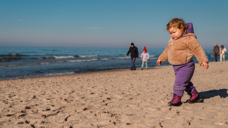 A young child in warm clothing strolls on the beach leaving footprints in the sand Families are seen...