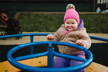 Child Enjoys Spinning on Playground Equipment in Vibrant Winter Attire During Sunny Afternoon.