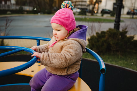 Child Enjoys Spinning on Playground Equipment in Vibrant Winter Attire During Sunny Afternoon.