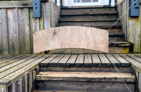 Wooden sign hanging above wooden stairs leading down to a patio area in a quiet outdoor setting.の写真素材