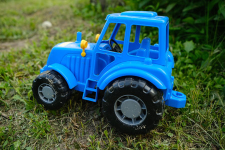 A bright blue toy tractor sits on a patch of green grass surrounded by foliage Sunlight highlights...