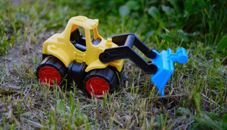 A vibrant yellow toy bulldozer is positioned on a patch of green grass showing its working scoop as...
