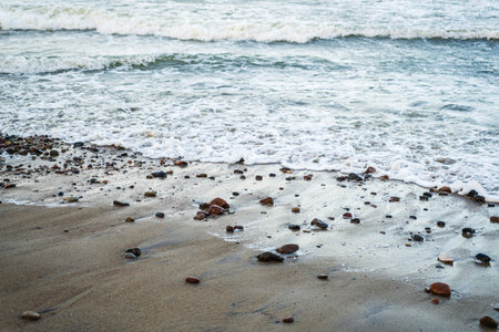 Waves softly roll onto a sandy beach scattered with smooth pebbles capturing the early morning light...