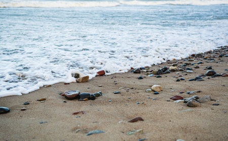 Waves softly roll onto a sandy beach scattered with smooth pebbles capturing the early morning light The shoreline creates a serene atmosphere perfect for reflection.の写真素材