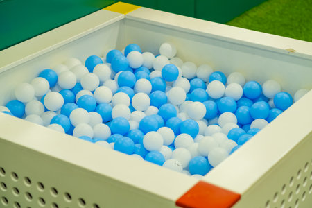 Bright blue and white balls fill a large square pit designed for kids to jump in and have fun. This playful zone is located indoors, providing a safe environment for energetic playの写真素材