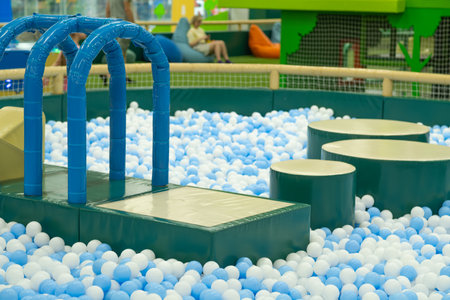 A vibrant indoor play space features a large ball pit filled with blue and white ballsの写真素材