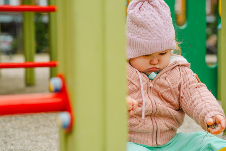 Toddler Playing in Sandbox Wearing Cozy Sweater and Hat at Playground During Sunny Day in Fall.の写真素材