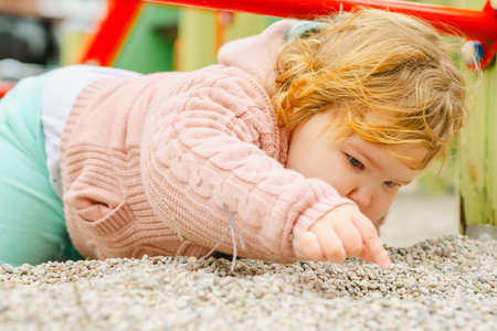 Toddler Playing in Sandbox Wearing Cozy Sweater and Hat at Playground During Sunny Day in Fall.の写真素材