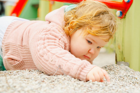 Toddler Playing in Sandbox Wearing Cozy Sweater and Hat at Playground During Sunny Day in Fall.の写真素材