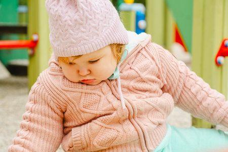 A young child wearing a knitted hat and cozy sweater explores a vibrant playground The setting features bright colors and a cheerful atmosphere perfect for outdoor fun.の写真素材