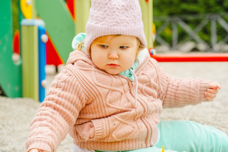 A young child wearing a knitted hat and cozy sweater explores a vibrant playground The setting features bright colors and a cheerful atmosphere perfect for outdoor fun.の写真素材