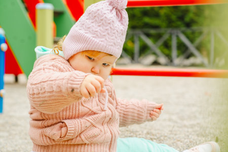 Toddler Playing in Sandbox Wearing Cozy Sweater and Hat at Playground During Sunny Day in Fall.の写真素材