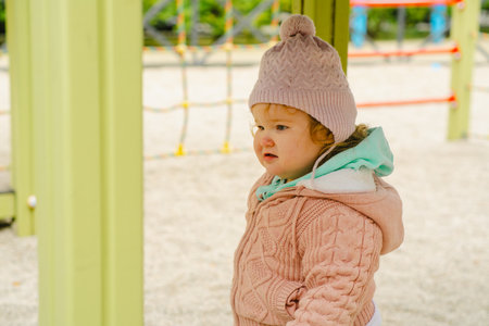 A young child wearing a knitted hat and cozy sweater explores a vibrant playground The setting features bright colors and a cheerful atmosphere perfect for outdoor fun.の写真素材