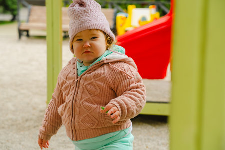 A young child wearing a knitted hat and cozy sweater explores a vibrant playground The setting features bright colors and a cheerful atmosphere perfect for outdoor fun.の写真素材
