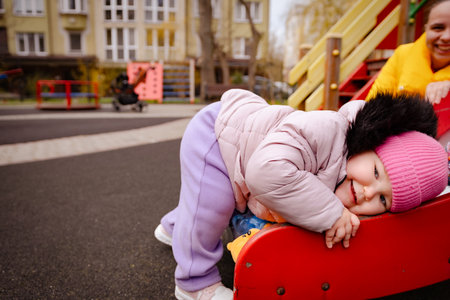 Child Enjoys Climbing on a Colorful Playground Slide During a Sunny Afternoon With a Parent Nearby.の写真素材