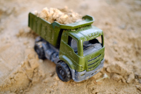 A toy dump truck rests on the sandy surface filled with sand showcasing vibrant colors against the natural earth Perfect for imaginative play outdoors inviting creativity.の写真素材