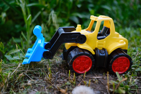 A vibrant yellow toy bulldozer is positioned on a patch of green grass showing its working scoop as it appears to be digging The sunny day adds to the playful atmosphere.の写真素材