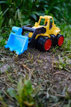 A vibrant yellow toy bulldozer is positioned on a patch of green grass showing its working scoop as...